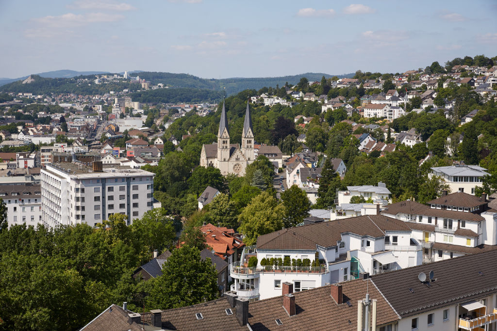 Luftansicht einer Stadt, im Zentrum steht eine Kathedrale, im Hintergrund sieht man Berge