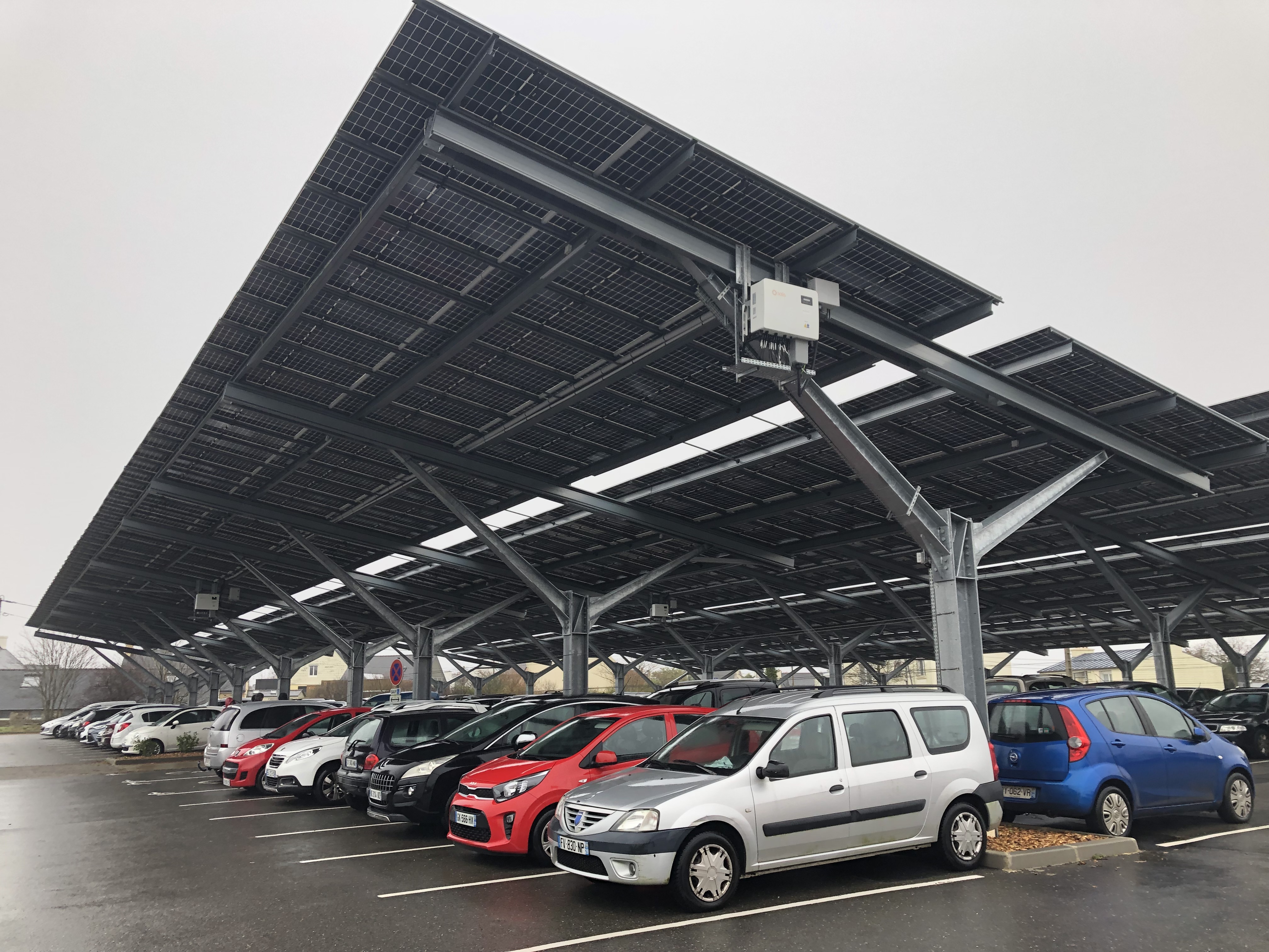 Auf einem mit Solaranlagen überdachten Parkplatz stehen Autos in mehreren Reihen. 