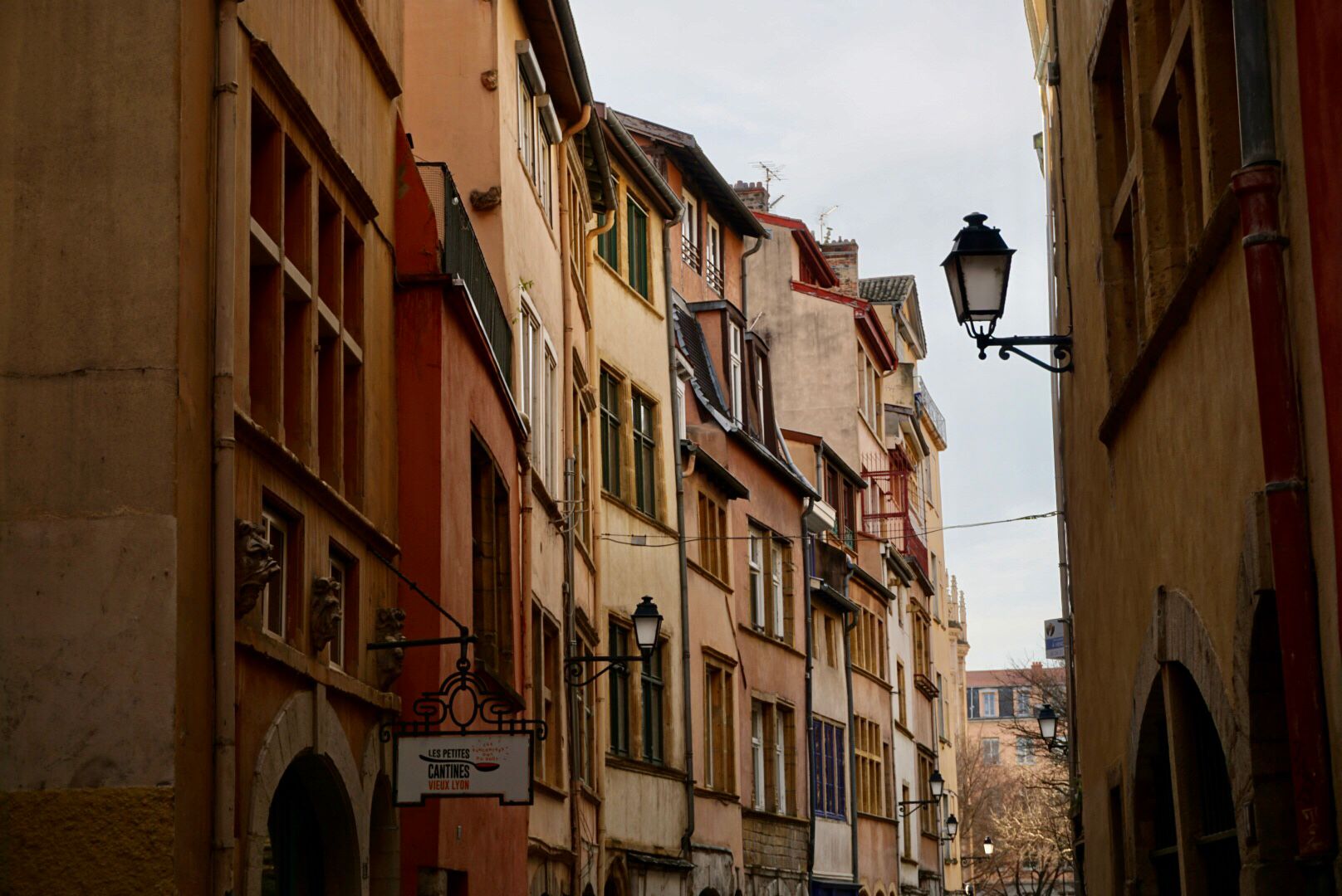 Schmale Straße, gesäumt von mehrstöckigen, farbenfrohen Altbauhäusern, mit Kopfsteinpflaster und einer klassischen Straßenlaterne