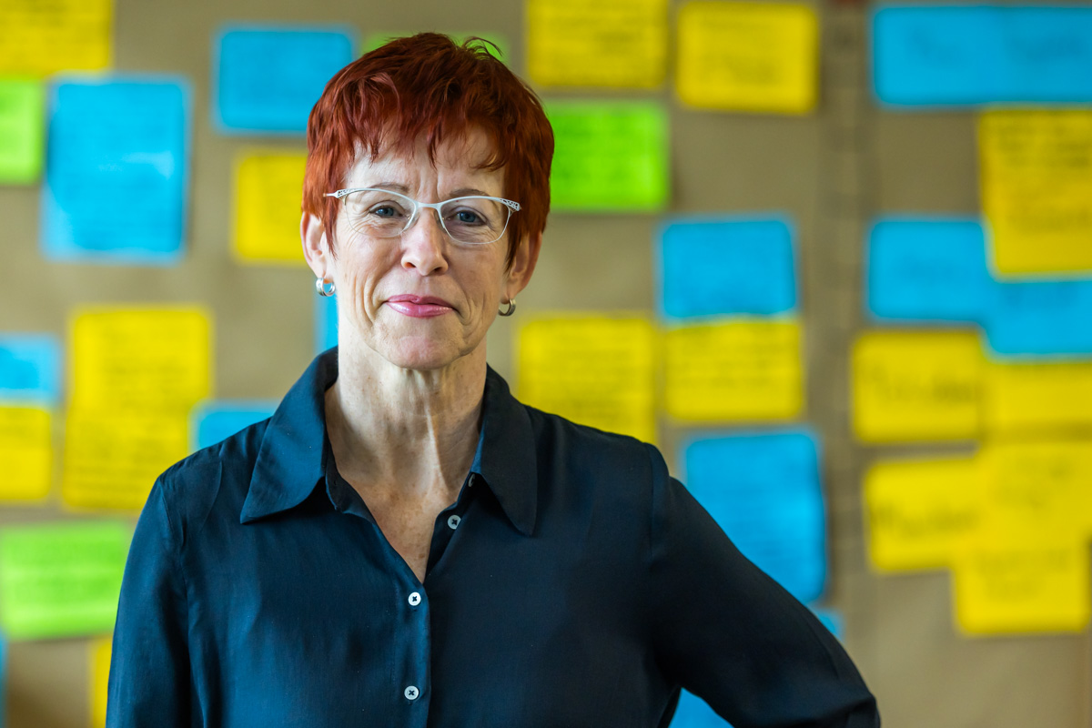 Porträtfoto von Grit Stillger, einer Frau mit kurzen rot-braunen Haaren, Brille und einer dunkle Bluse.