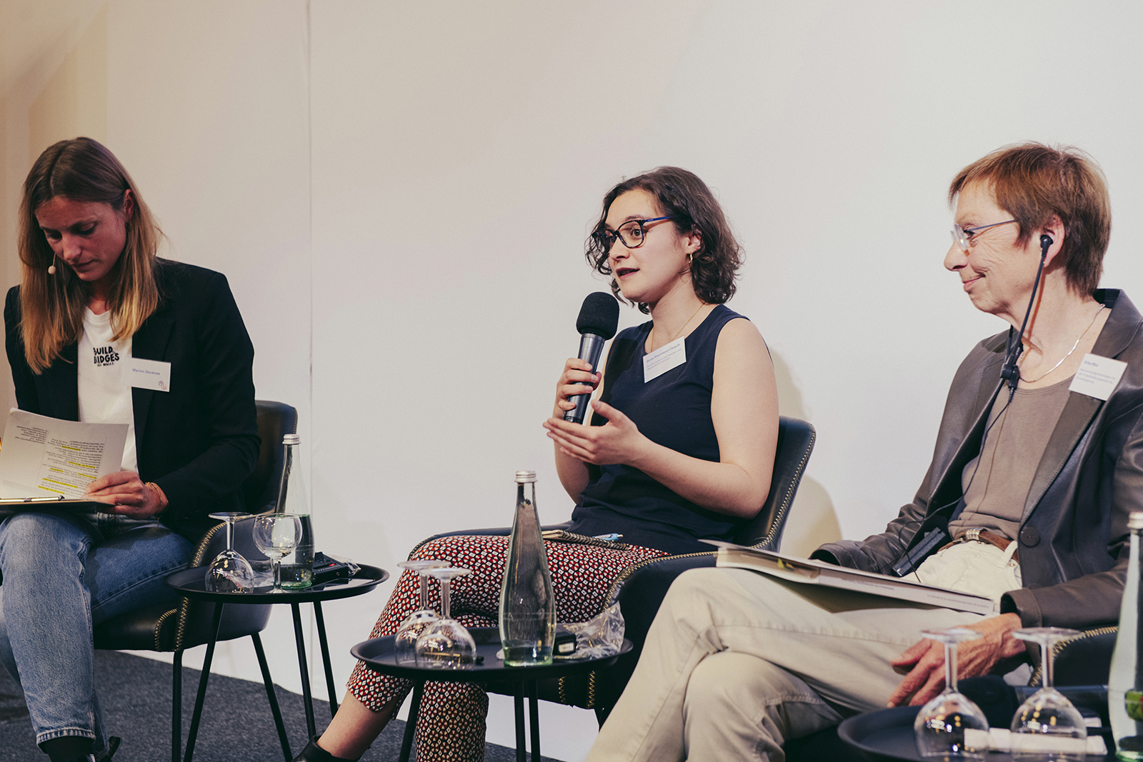 Eine Frau spricht am Mikrofon, umgeben von zwei anderen Frauen in einer Podiumsdiskussion