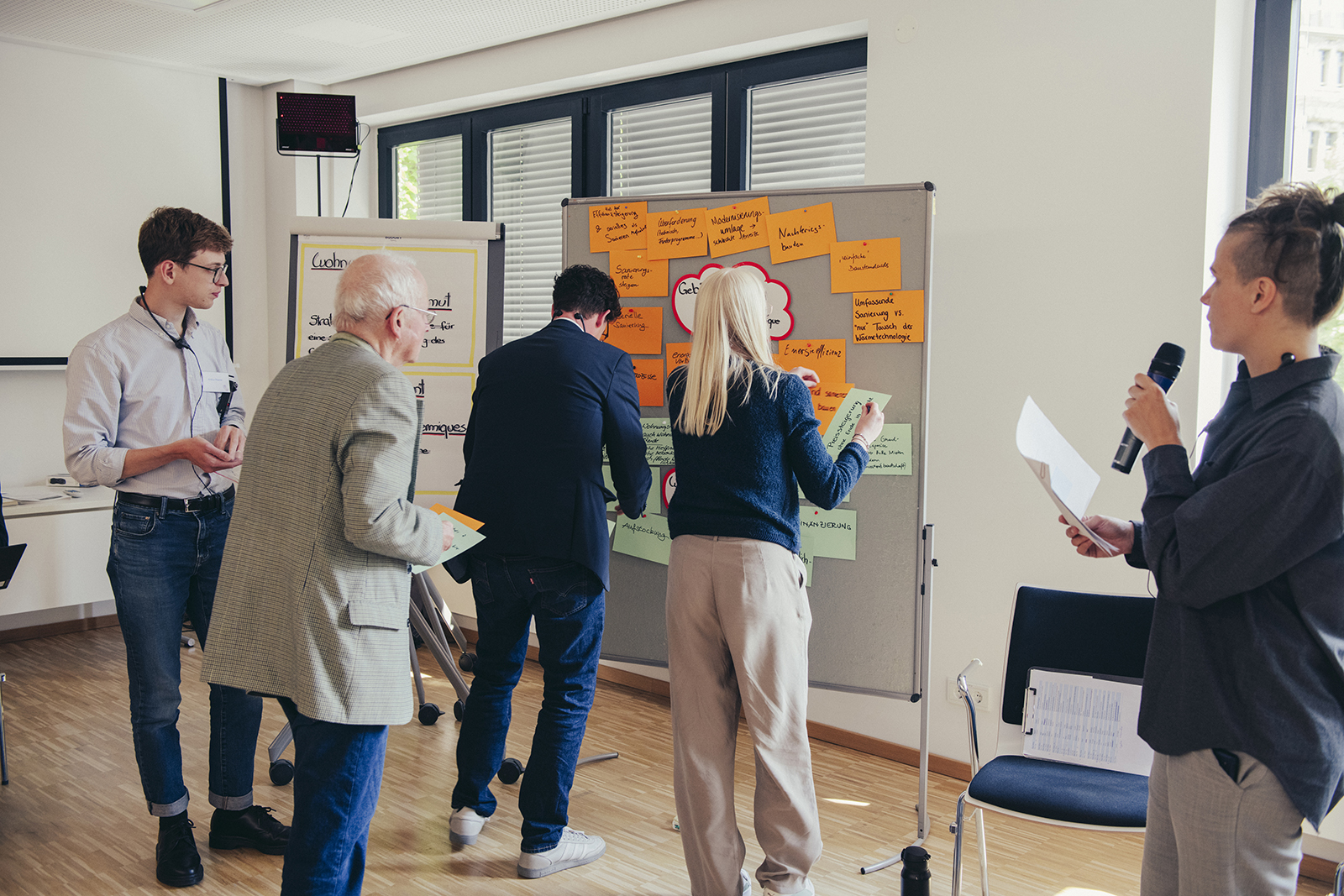 Personen nehmen während eines Workshops aktiv teil, indem sie thematische Post-its an eine Tafel heften