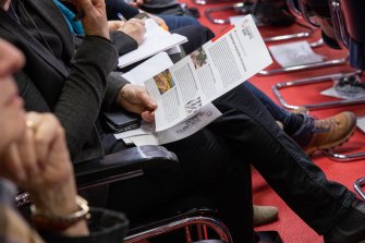 Eine Person sitzt in einem Konferenzsaal und hält ein Dokument in der Hand.