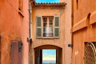 Ein altes, terracottafarbenes Haus, dahinter sind man das Meer.