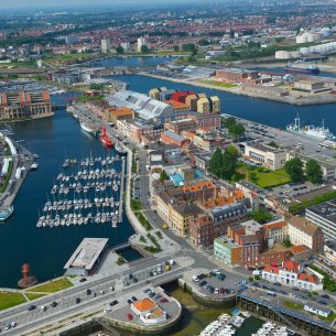 Luftaufnahme: Industriegebäude, Wohn- und Bürohäuser umgeben einen Hafen.
