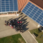 Eine Gruppe von Menschen steht vor einem Gebäude mit Unterstand, auf deren Dächern Solarzellen angebracht sind.