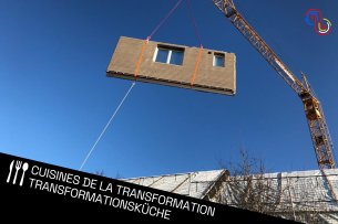 Eine vorgefertigte Wand wird von einem Krahn an eine Fassade angebracht