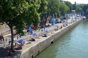 Blick auf das Ufer der Seine: Einige Menschen liegen unter Sonnenschirmen, andere flanieren auf einer autofreien Straße.