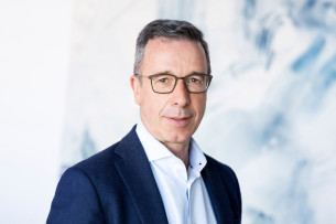 Person mit kurzen dunkelgrauen Haaren und Brille. Sie trägt ein weißes Hemd und dunkelblaues Jackett.